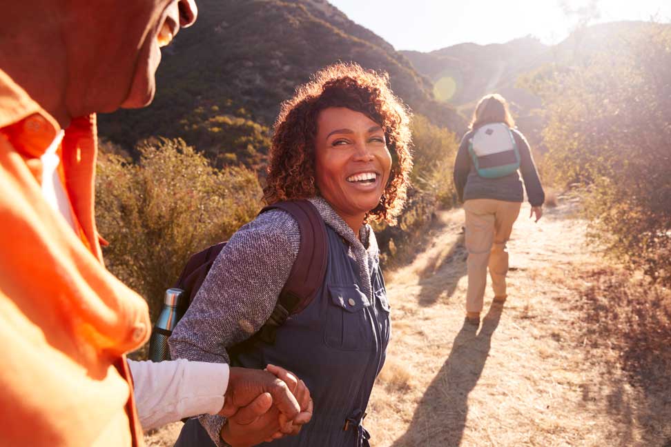 three people walking on a hiking trail with a woman facing the camera and smiling