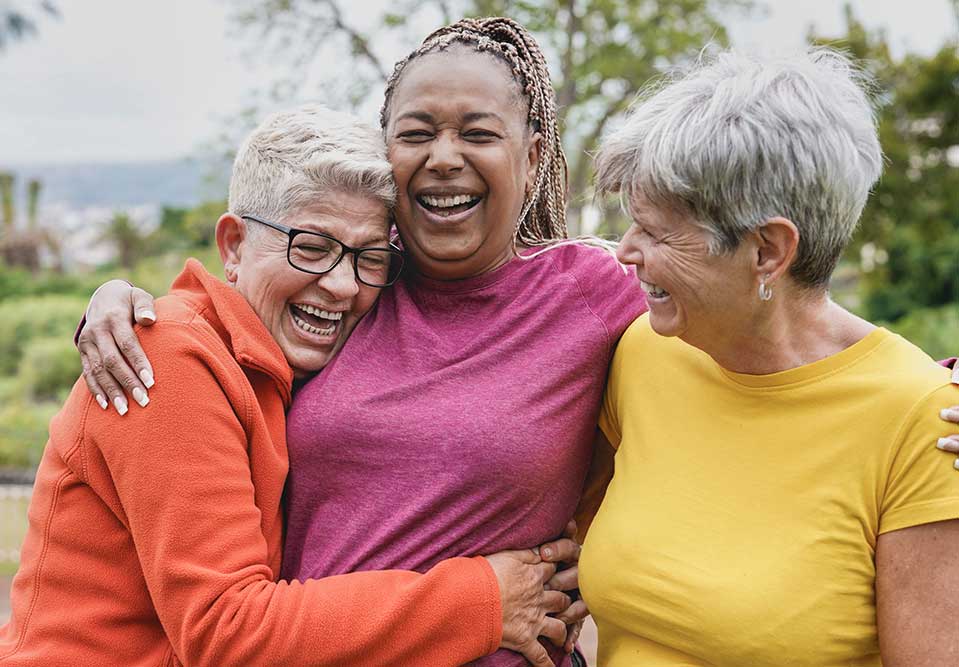 three older women hug and smile