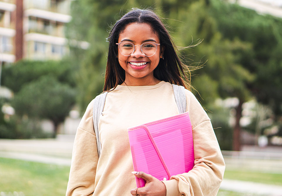 a teen girl holding a notebook smiles at the camera